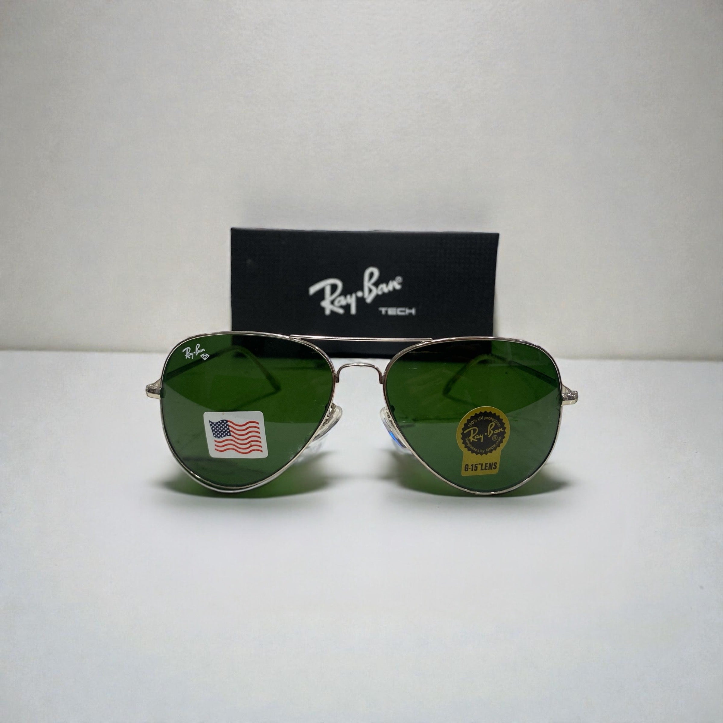 Front view of Ray-Ban Aviator sunglasses with green lenses and silver frame on white surface with black Ray-Ban Tech box behind