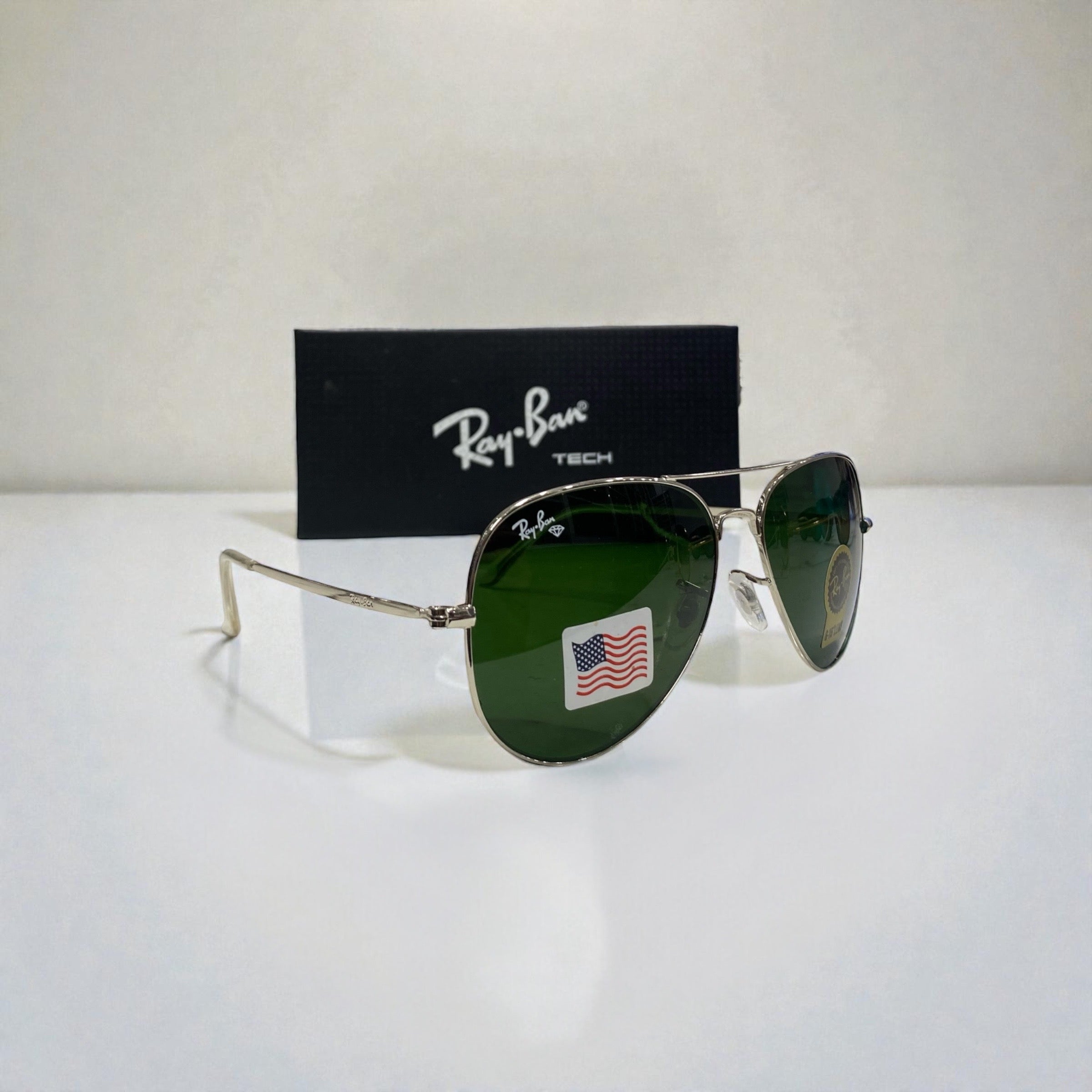 Ray-Ban Aviator sunglasses with silver frame and green lenses angled sideways on white surface with black Ray-Ban Tech branded box behind