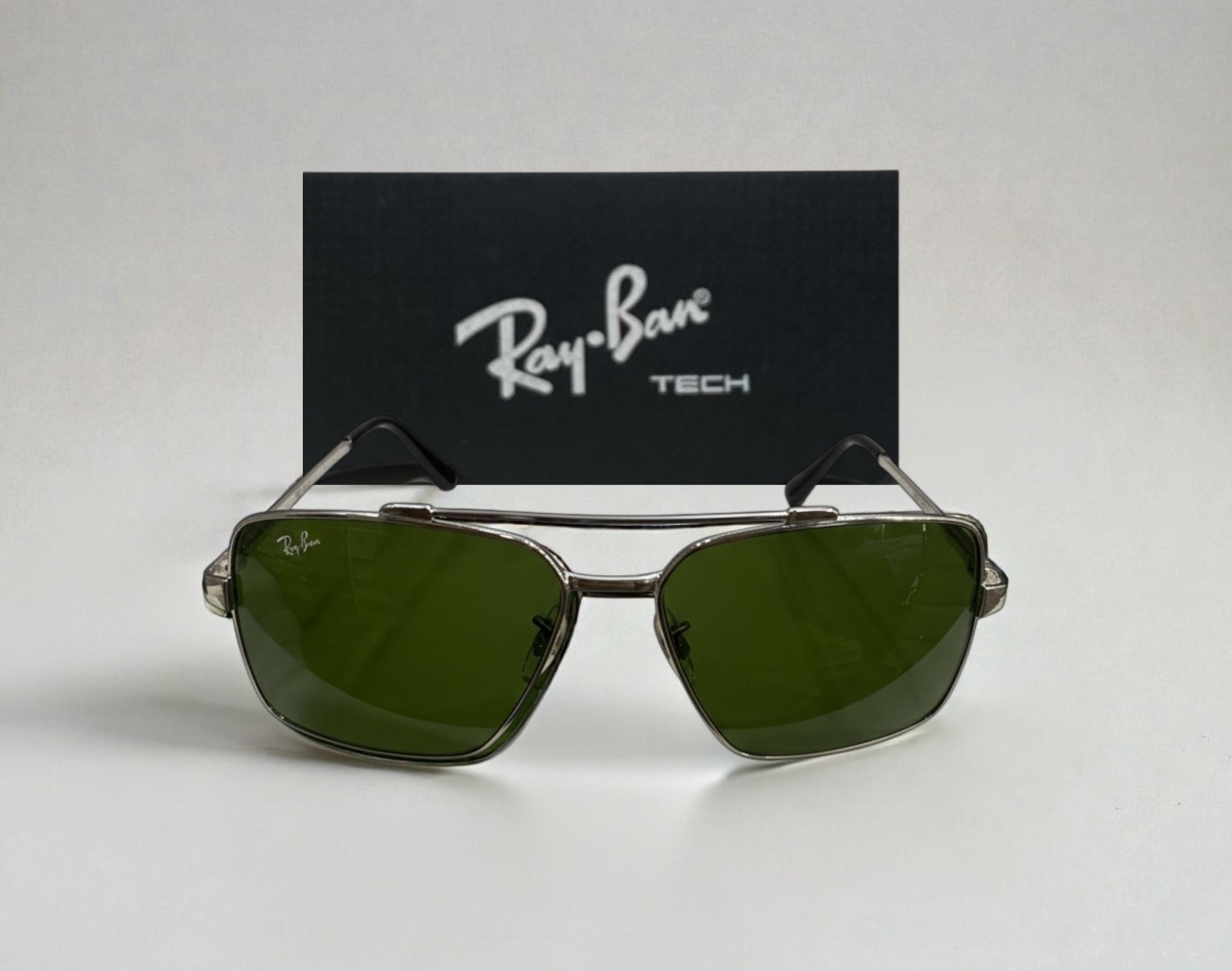 Close-up front view of Ray-Ban Tech square sunglasses with green lenses and metal frame positioned in front of Ray-Ban Tech logo background