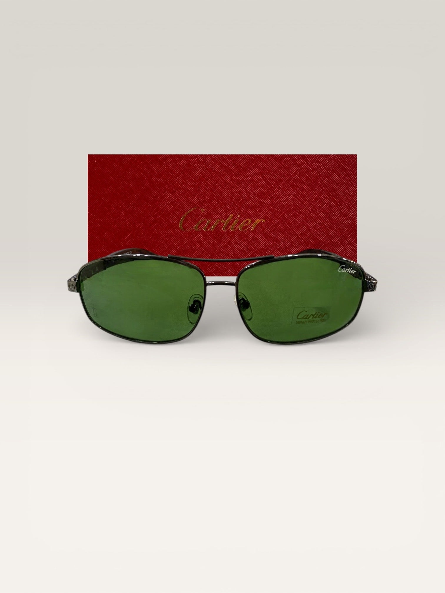 Front view of Cartier rectangular green lens sunglasses with metal frame positioned against red Cartier branded case