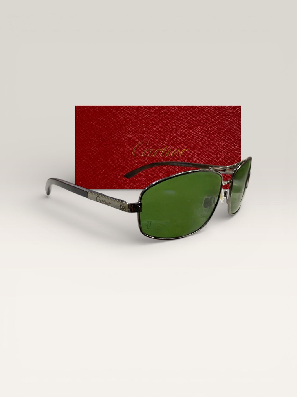 Side view of Cartier luxury sunglasses with green lenses and metal frame resting in front of red Cartier branded case