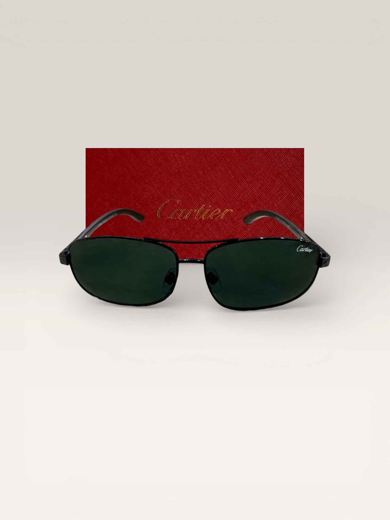 Front view of Cartier black metal frame sunglasses with green lenses in front of a red Cartier case