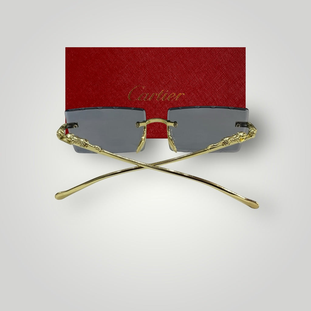 Top view of Cartier rectangular dark lens sunglasses with crossed gold textured arms and red Cartier box in the background
