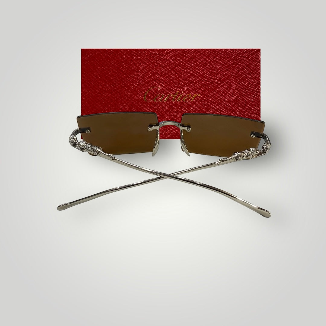 Back view of luxury rimless sunglasses showing silver detailed temples crossed, with red Cartier case background.