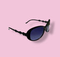 Beenai Original women sunglasses angled view showing black wavy frame and gradient blue lenses on pink background